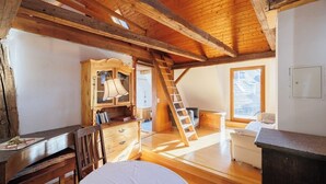 Une chambre mansardée chaleureuse avec des poutres apparentes, une armoire en bois, un bureau et une échelle.