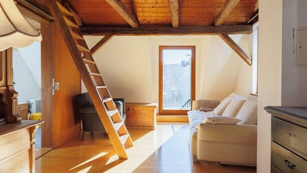 Une chambre de style « loft », avec une échelle en bois, un canapé blanc et une grande fenêtre.