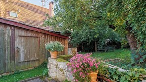 Une clôture en bois rustique, un mur de pierres agrémenté de plantes en pot et un jardin luxuriant aux fleurs roses.