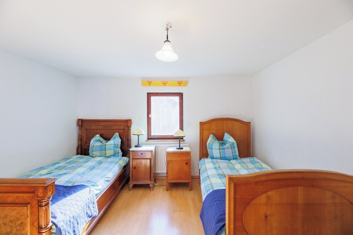 Ein Schlafzimmer mit zwei Holzbetten, einem Fenster, einer Heizung und einer Pendelleuchte.