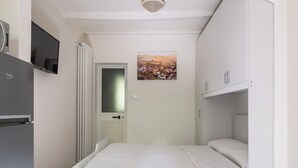 A compact room with a bed, a small kitchenette, and a door leading to a bathroom. - Studio Fondazza 22 by Wonderful Italy (Bologna)