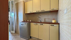 Cocina compacta con armarios color crema, lavavajillas de acero inoxidable y salpicadero azulejado.