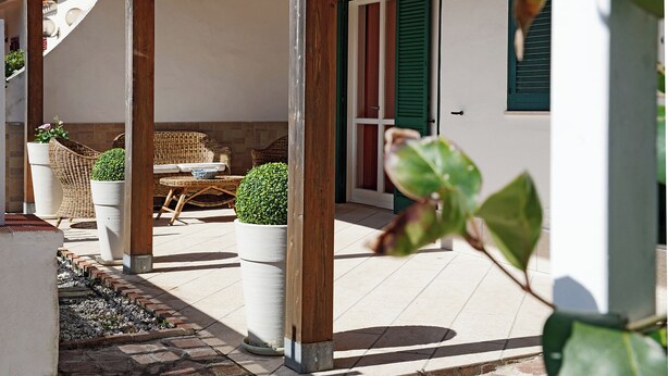 Un espacio de estar al aire libre con techo, muebles de mimbre y plantas en macetas.