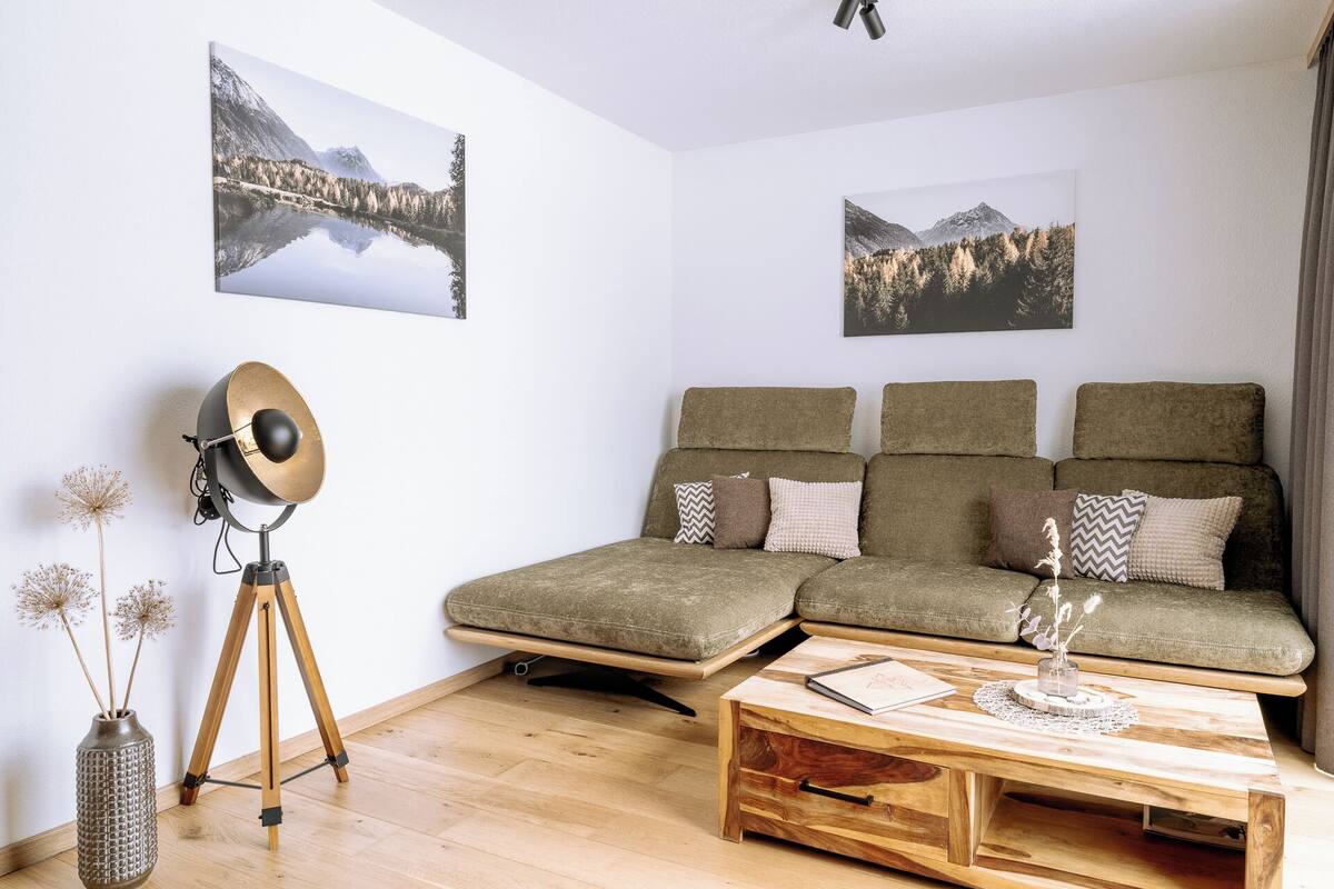 A modern living room with a sectional sofa, a wooden coffee table, and two wall-mounted pictures of a mountain landscape.