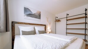 A neatly made bed with white linens and a wooden headboard, a wall-mounted shelf unit, and a framed picture above the bed. - Apart Peak Ötztal  (Laengenfeld)