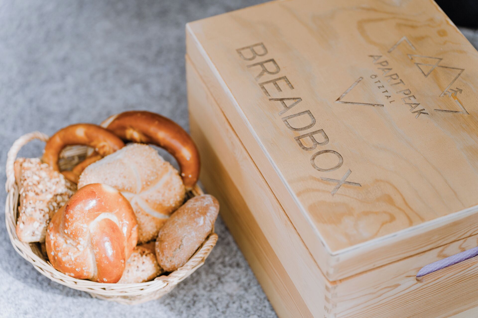 A wooden box labeled "BREADBOX" with a basket of bread and pretzels beside it.