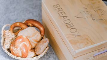 A wooden box labeled "BREADBOX" with a basket of bread and pretzels beside it.