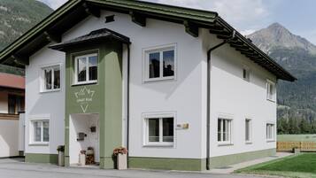 A two-story building with a green and white facade, a sign indicating 'APART PEAK', and a mountain backdrop.