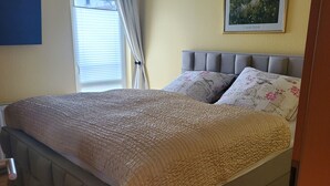 Un dormitorio con cama, ventana con cortinas, un cuadro en la pared y una puerta.