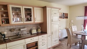 Una cocina con armarios blancos, un fregadero, un tostador y un hervidor. Hay una mesa de comedor con sillas y un florero.