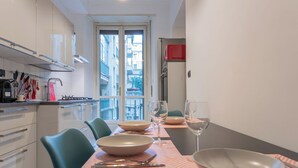 A modern kitchen with a dining table set for four, featuring a view of the city through large windows.