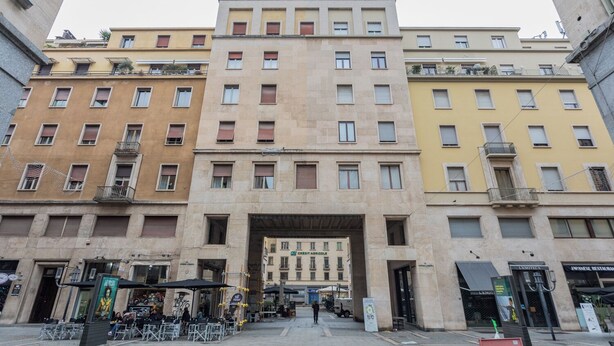 A multi-story building with a central entrance, balconies, and various storefronts at the ground level.