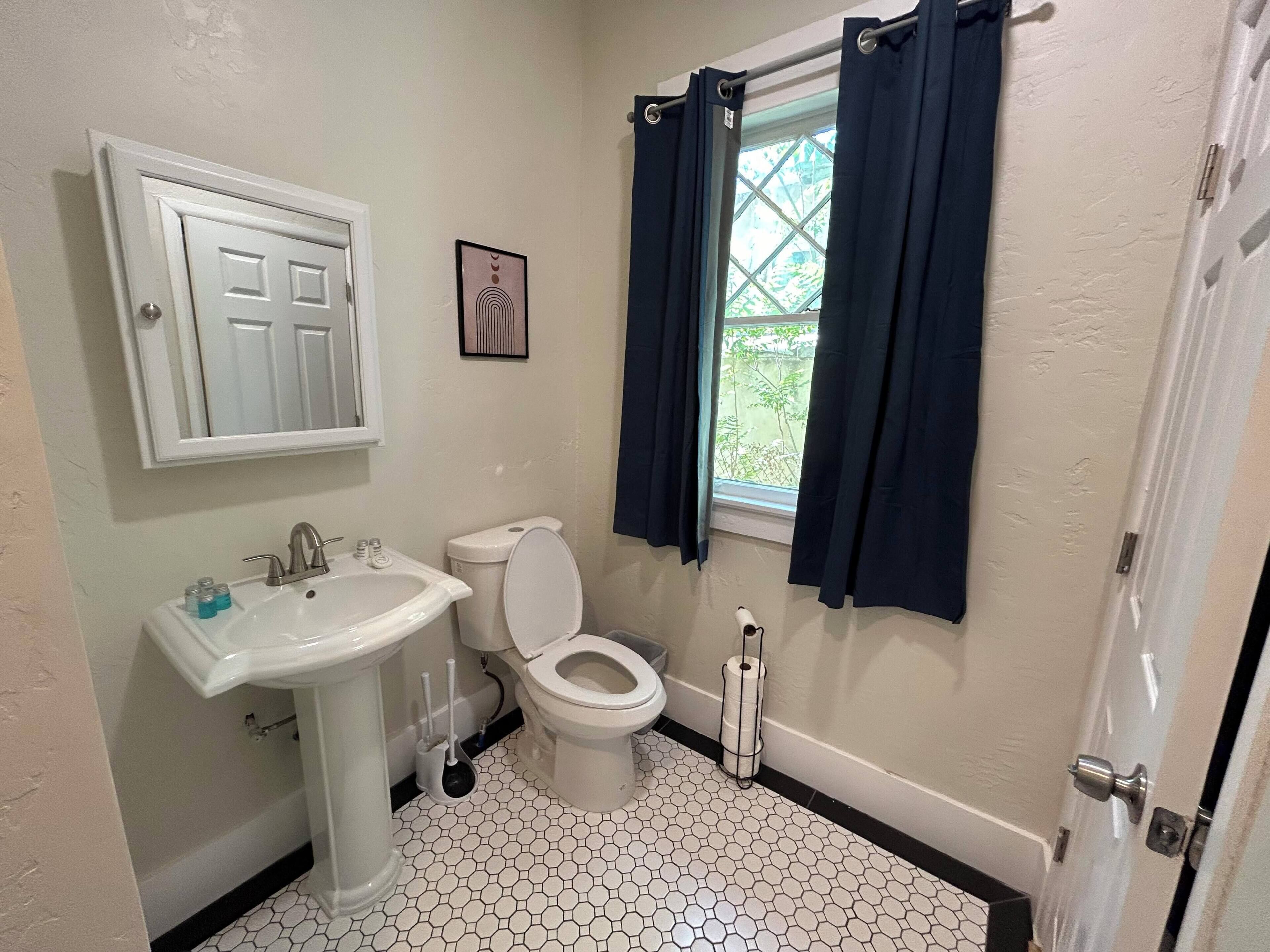 Une salle de bain avec un lavabo blanc, des toilettes et une fenêtre ornée de rideaux foncés.