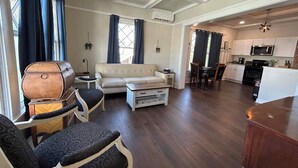 Un amplio espacio de sala con sofá, sillones, una mesa de centro y un barril de madera. Hay un comedor con mesa y sillas, y una cocina equipada con microondas y estufa.