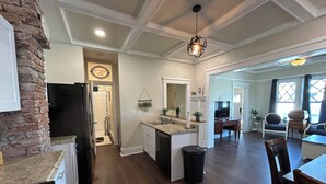 Una cocina amplia con una isla central, un comedor con mesa y sillas, y una sala de estar con sofá y televisor.