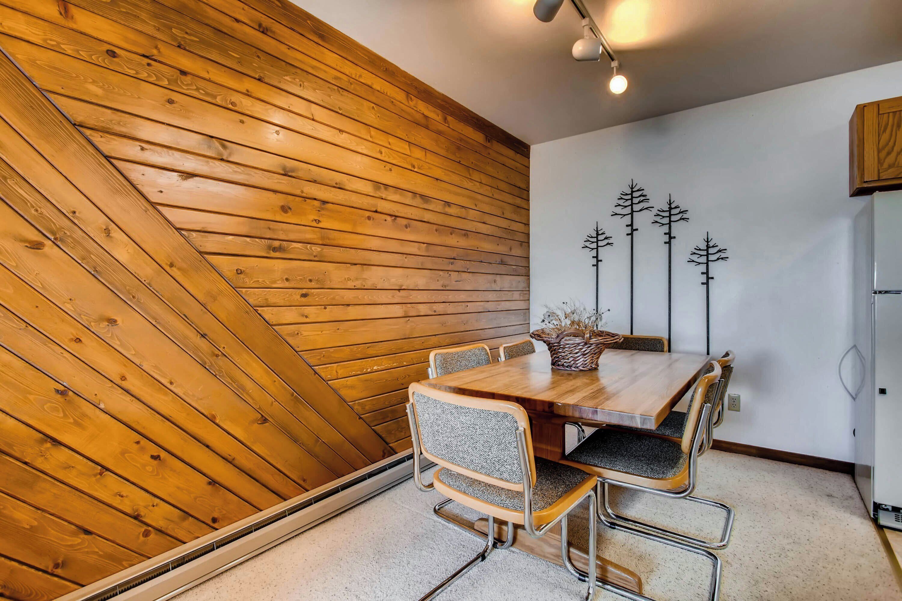 Un espace repas doté d’un plafond en bois à pente, d’une table à manger en bois et de quatre chaises rembourrées.
