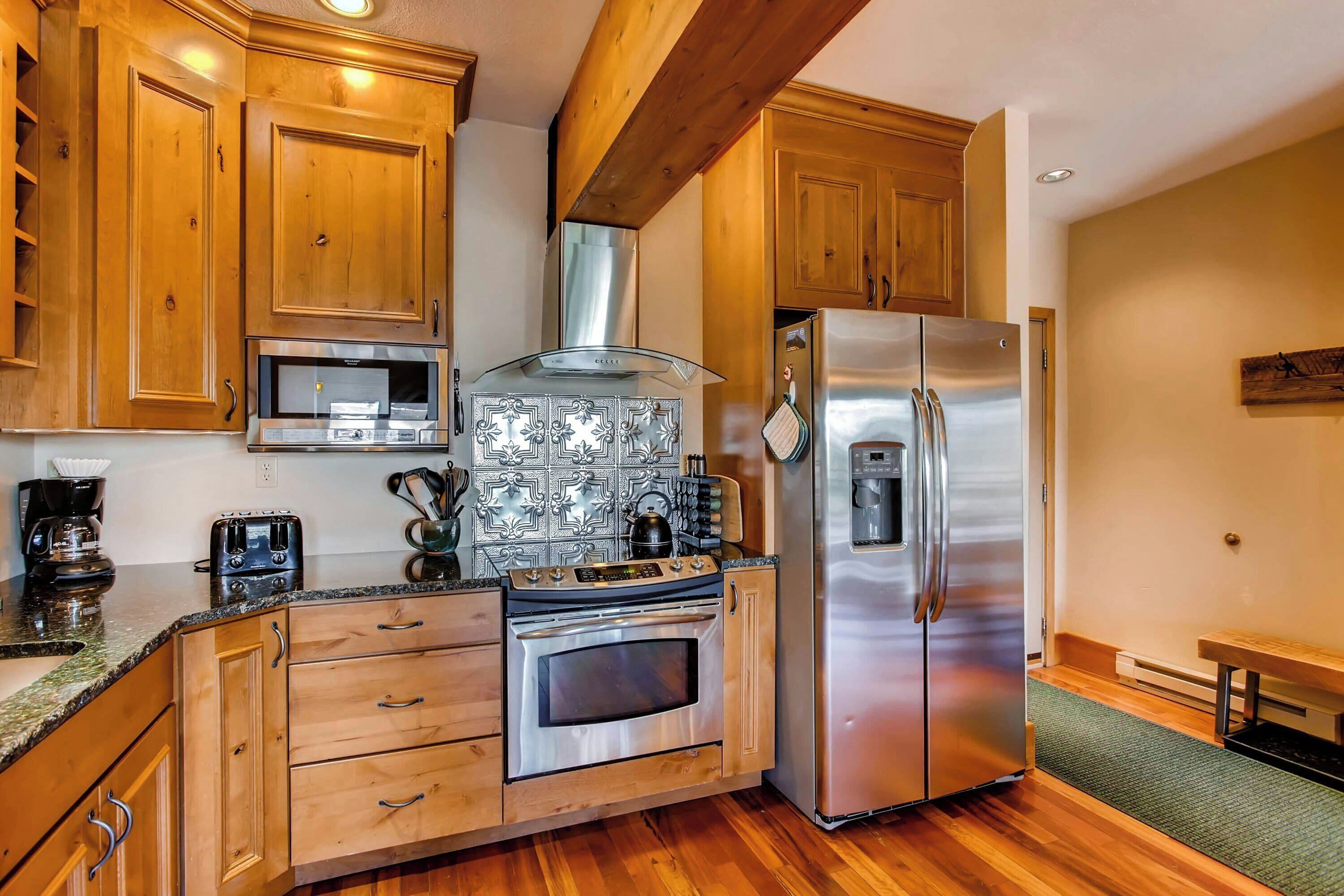A kitchen with wooden cabinets, a stainless steel refrigerator, a microwave, and a stove.