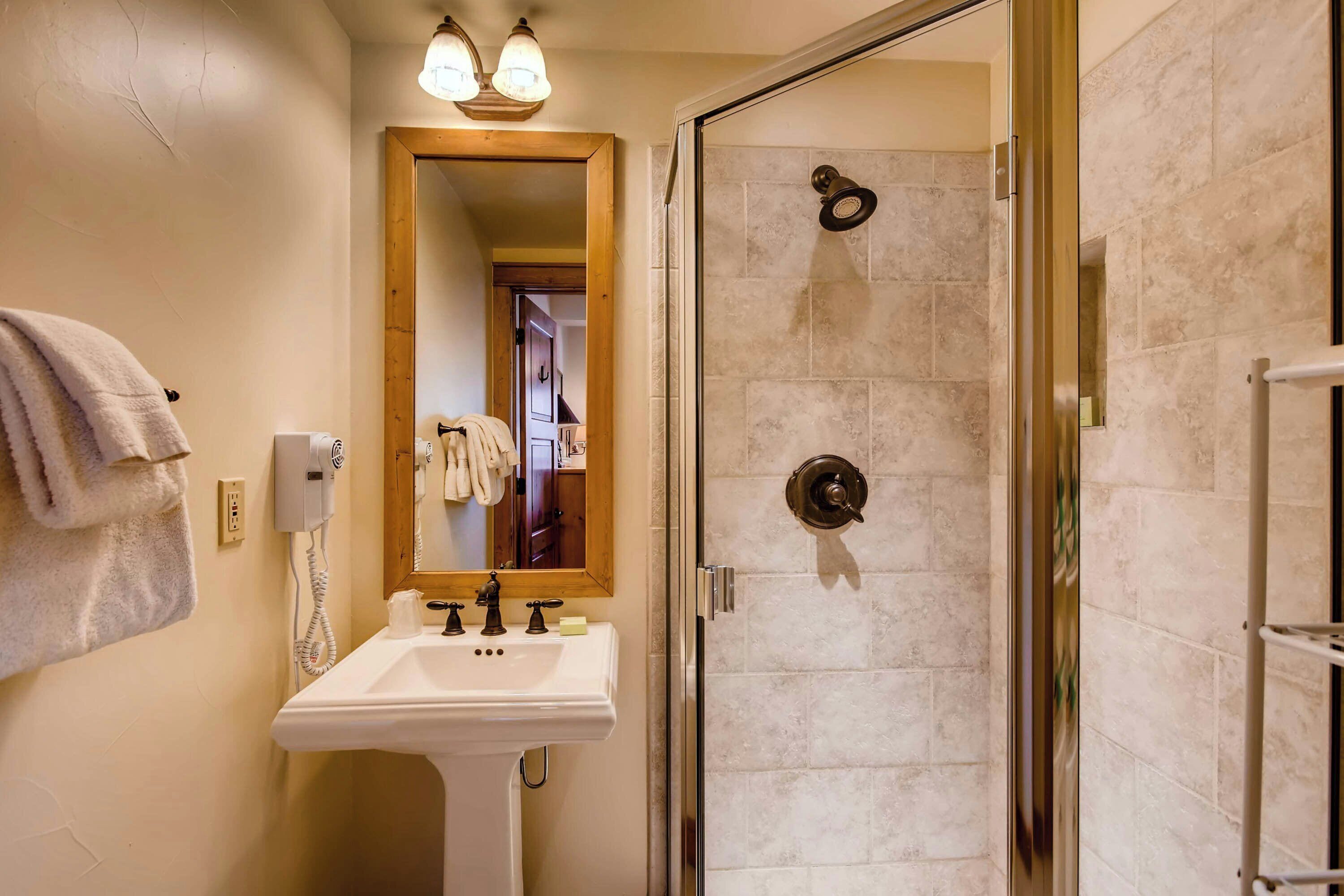 Une salle de bain équipée d’un lavabo, d’un miroir, d’un porte-serviettes et d’une douche à parois de verre.