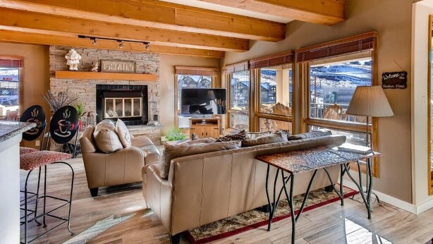 A cozy living room with a fireplace, a sofa, a TV, and large windows offering a mountain view. - Crested Butte Mountain Resort Properties by Vail Resorts (Crested Butte)