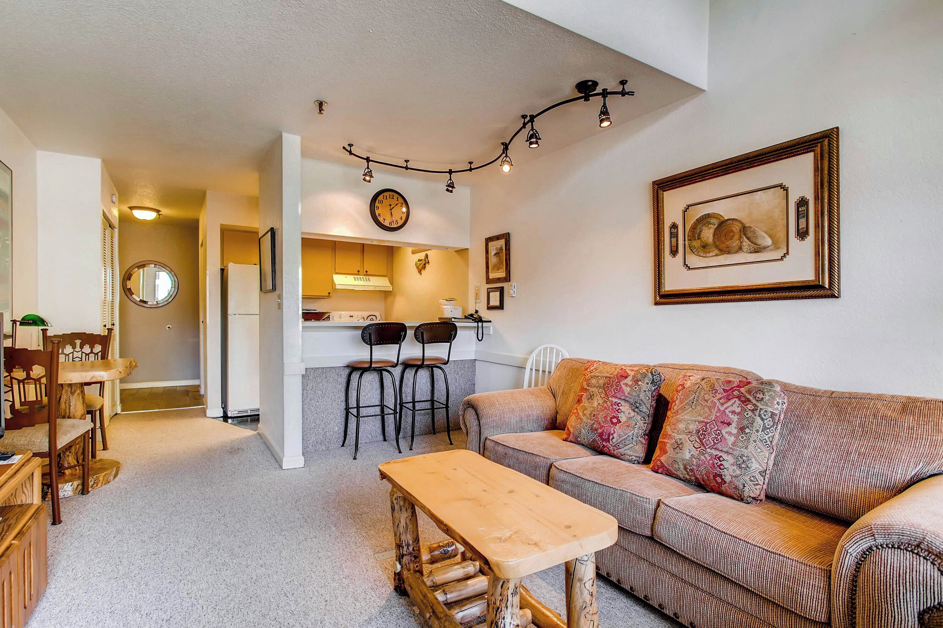 A cozy living room with a sofa, a wooden coffee table, and a kitchen area in the background.