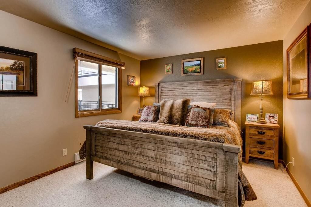 A bedroom with a wooden bed, a window with a view, and a nightstand with a lamp.