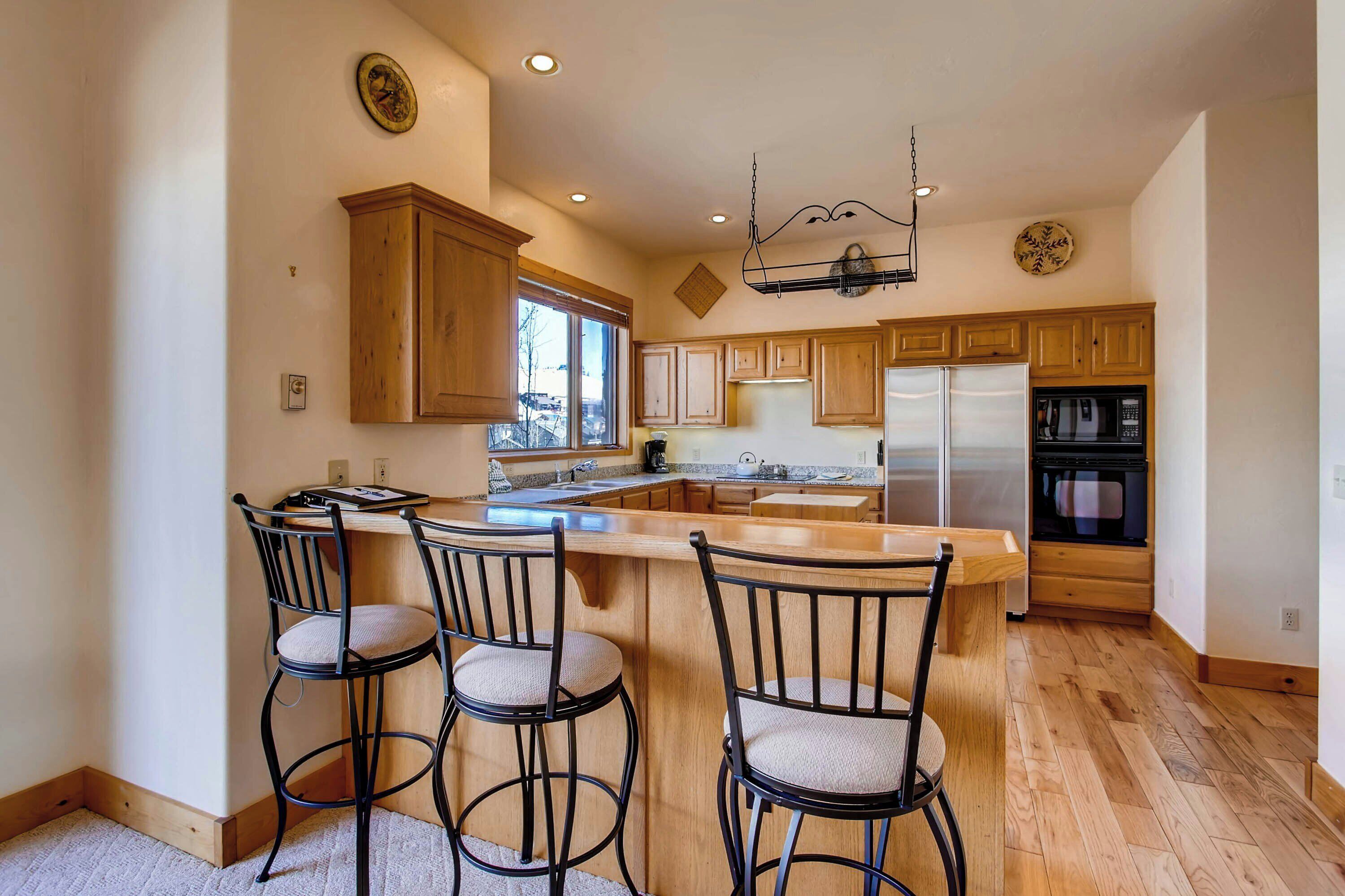 A modern kitchen with wooden cabinets, a central island with bar stools, stainless steel appliances, and a hanging light fixture.