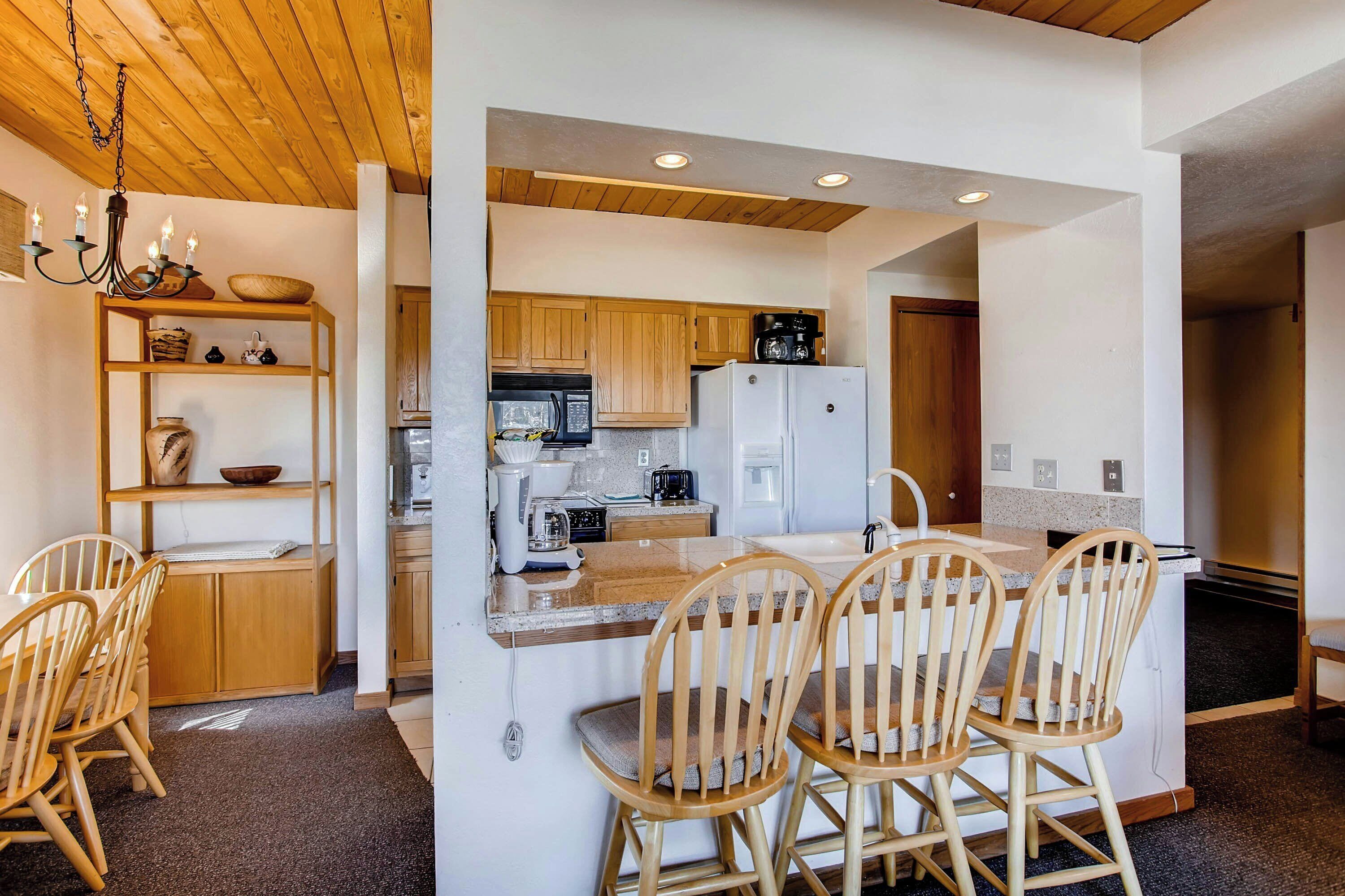 A modern kitchen with wooden cabinets, a white refrigerator, and a dining area with wooden chairs.