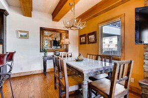 A dining area with a wooden table and chairs, a chandelier, and a large window with a view of buildings. - Crested Butte Mountain Resort Properties by Vail Resorts (Crested Butte)