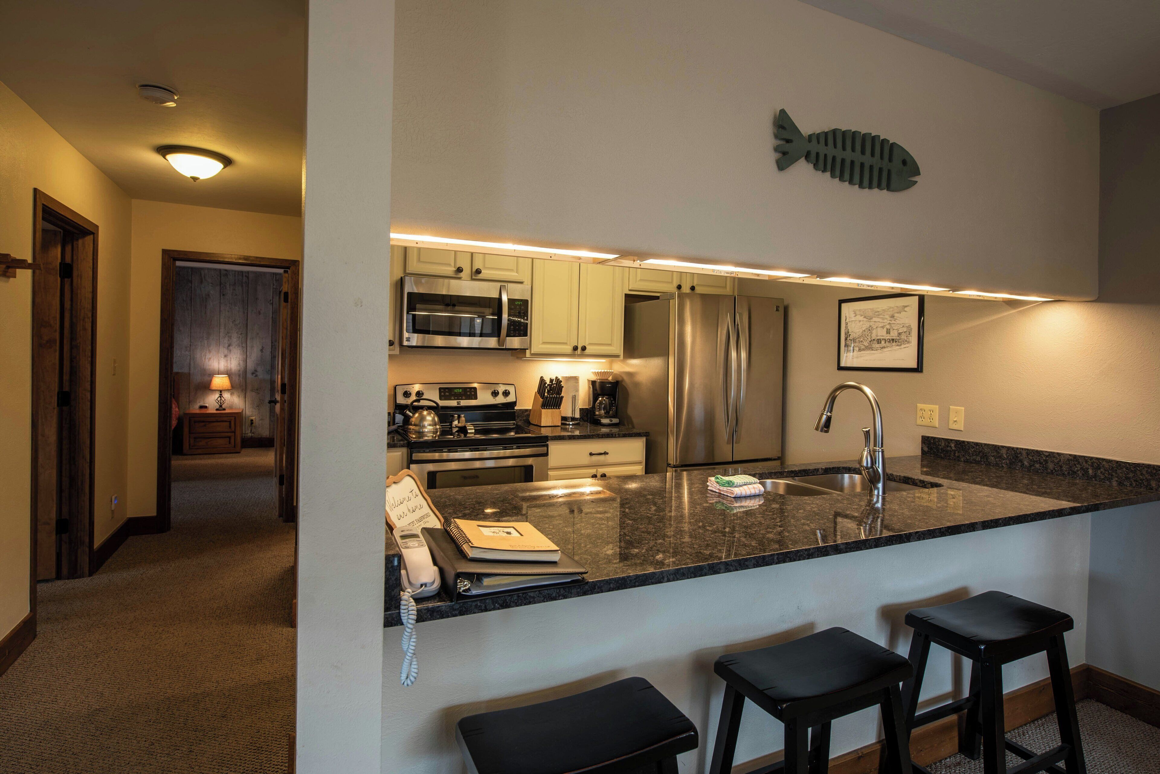A modern kitchen with granite countertops, stainless steel appliances, and a fish-themed wall decoration.