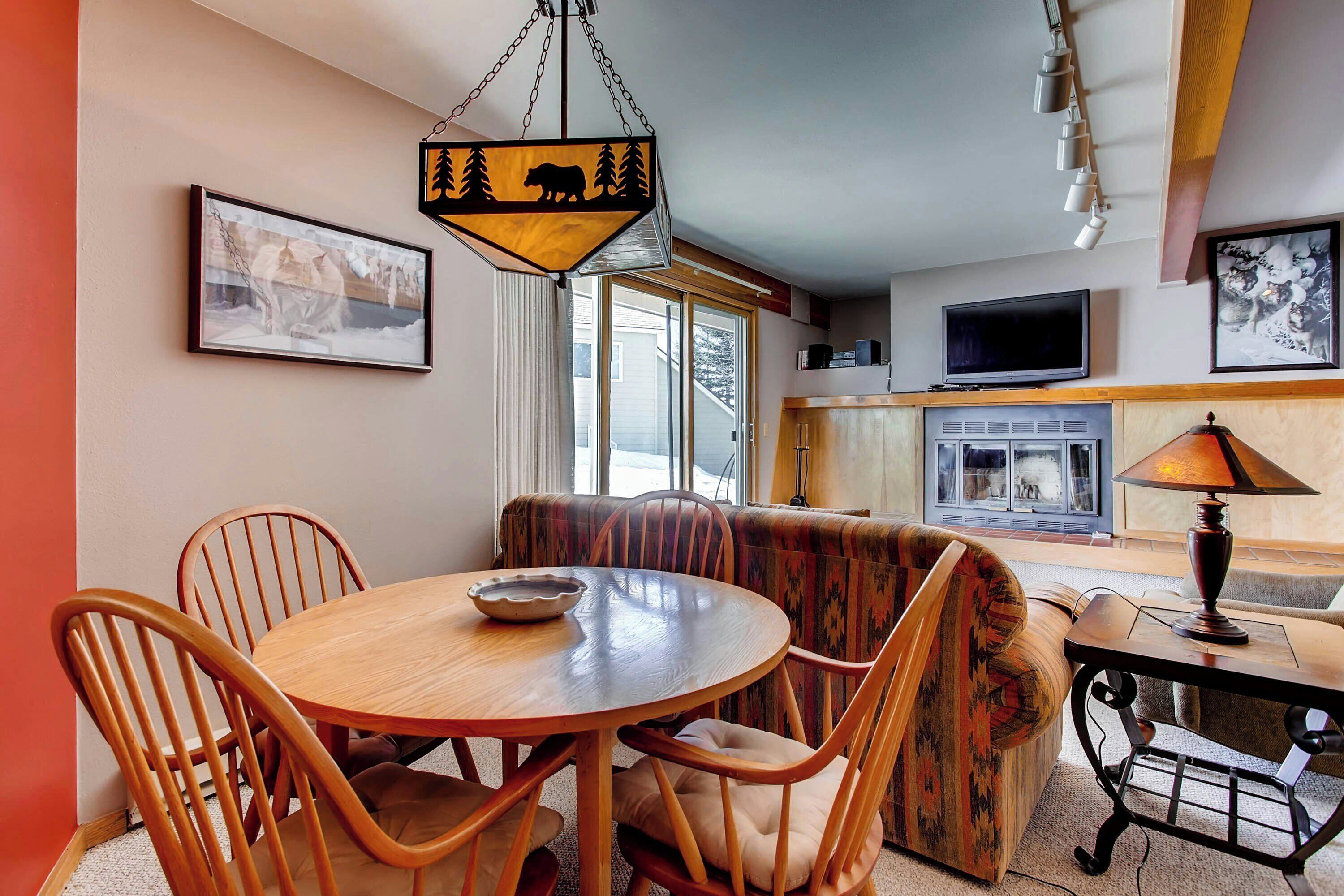 A dining area with a wooden table and chairs, a sofa, and a television in the background.