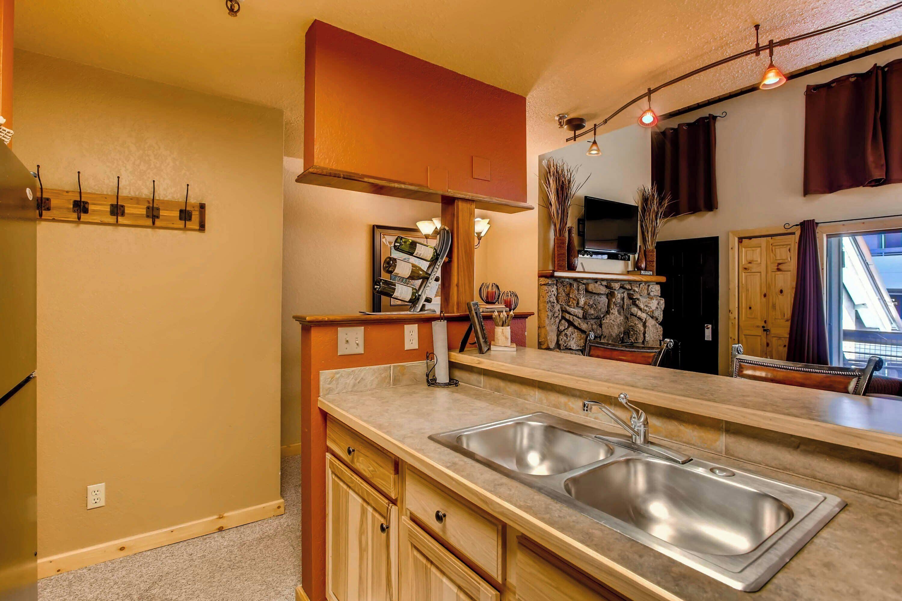 A kitchen with a double sink, wooden cabinets, a stone accent wall, and pendant lighting.