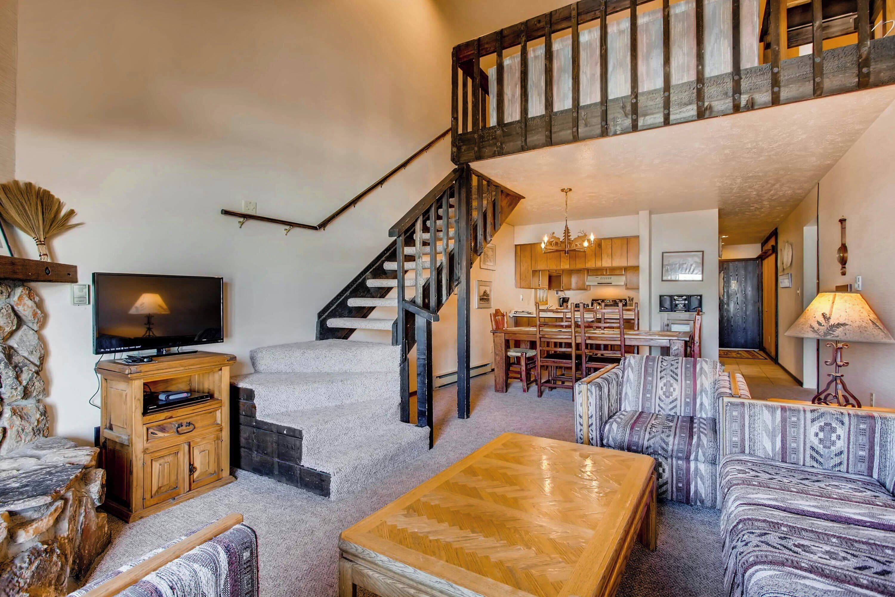 A spacious living area with a staircase, wooden furniture, and a television.