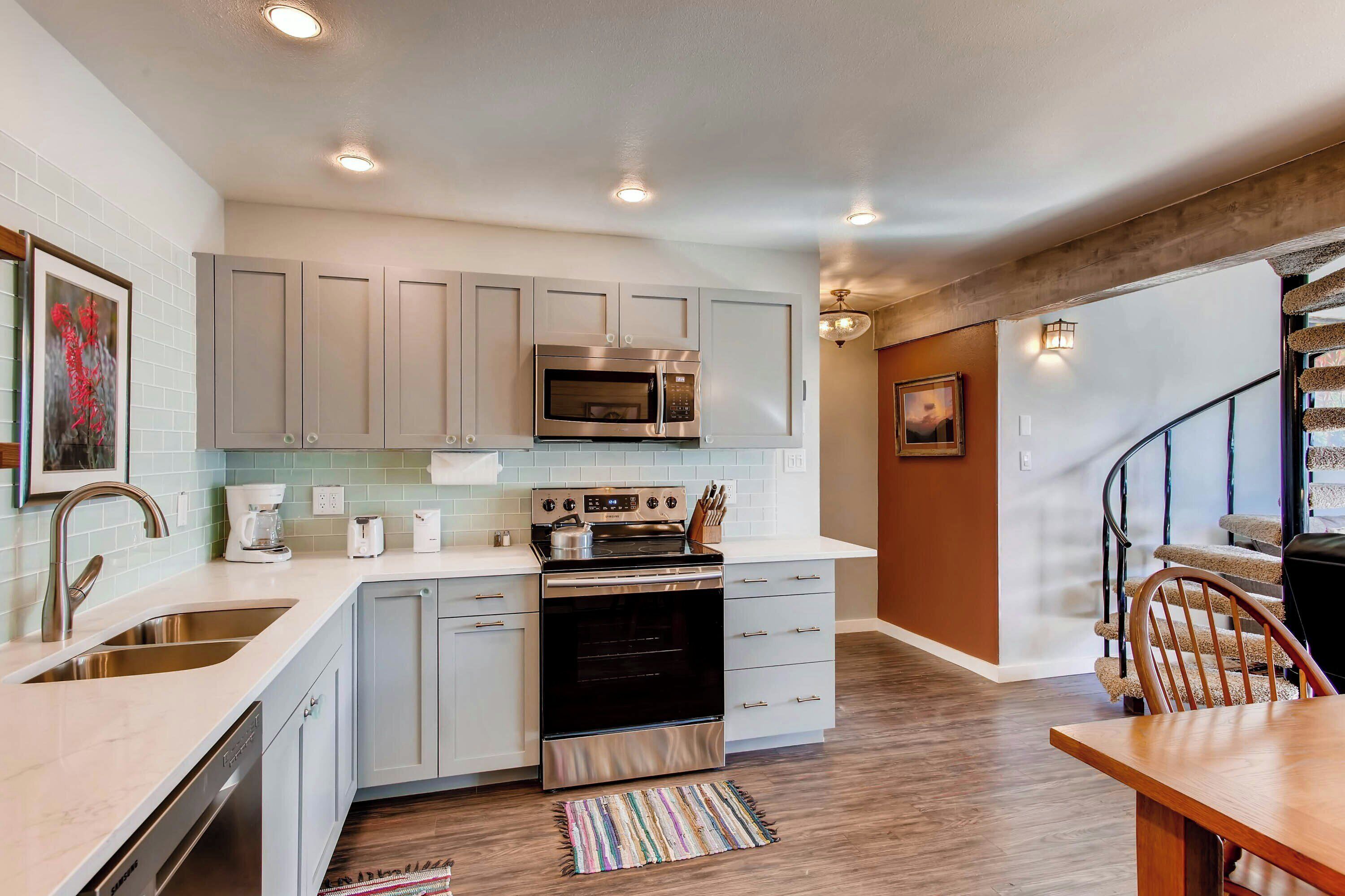 A modern kitchen with grey cabinets, stainless steel appliances, and a wooden dining table.