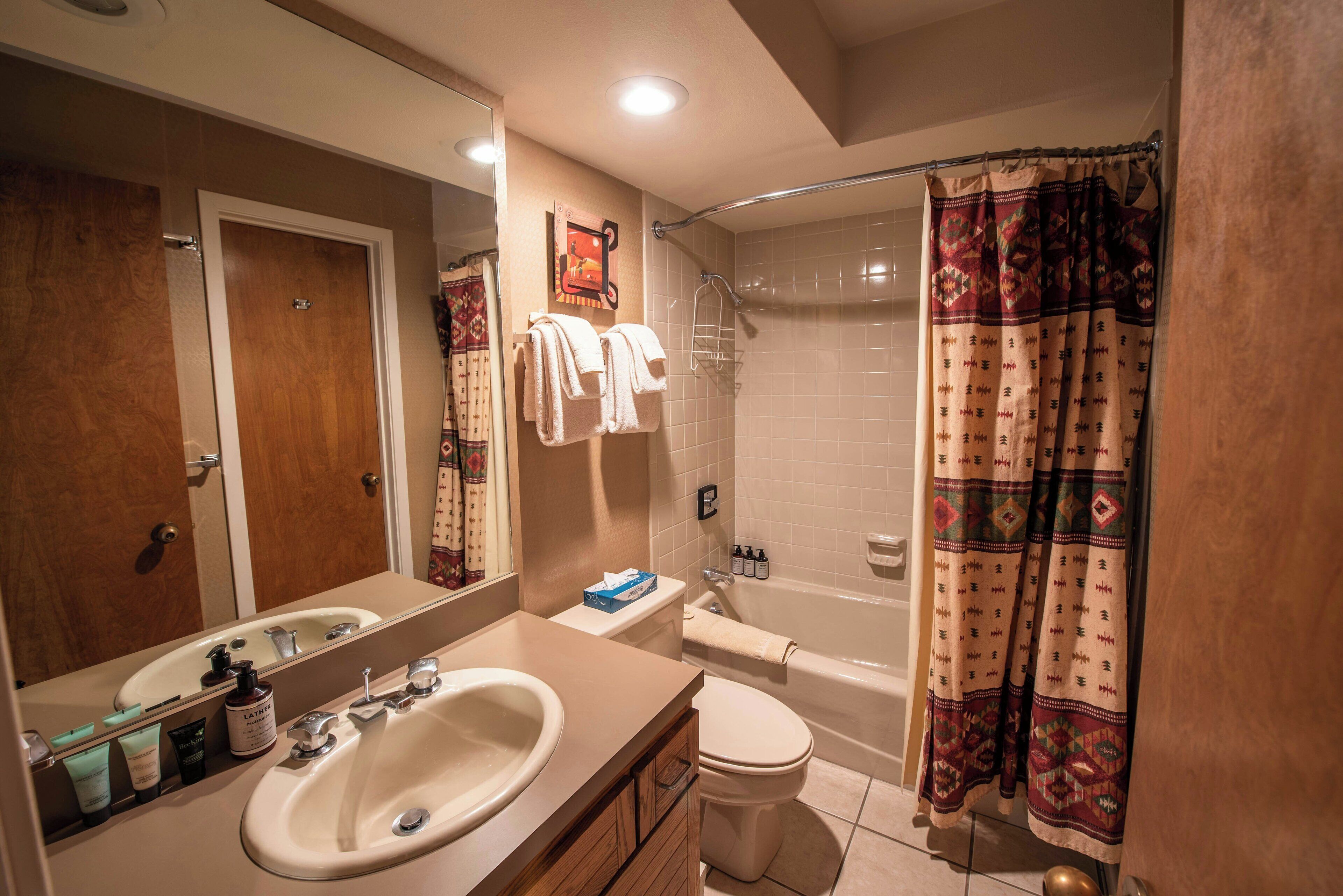 A bathroom with a sink, toilet, and shower. There are towels hanging on the wall and a shower curtain.