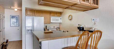 A kitchen with wooden cabinets, a refrigerator, a microwave, and a stove. There are two wooden chairs at the kitchen island.