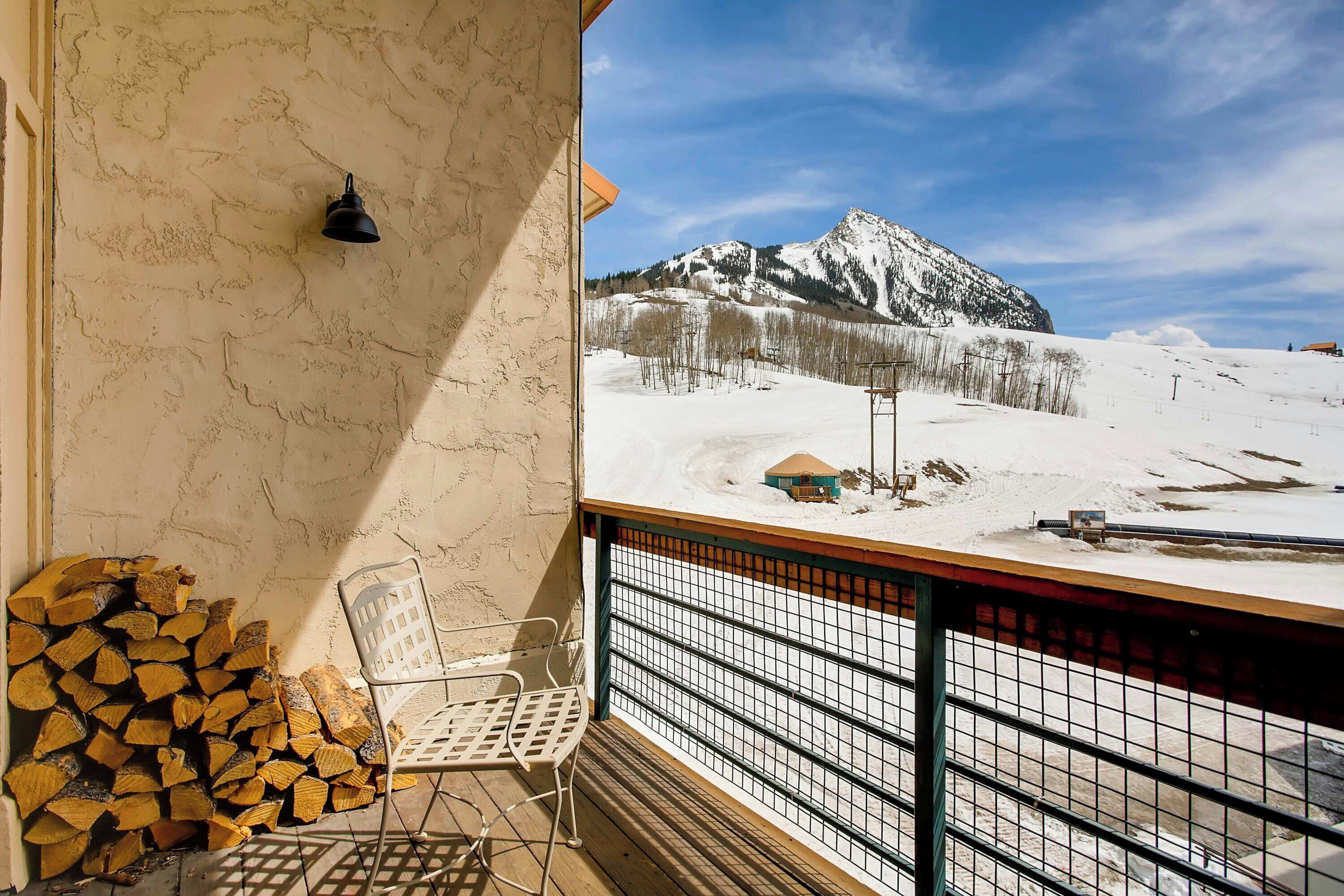 A balcony with a view of a snow-covered mountain, a chair, and a stack of firewood.