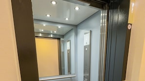 Ein Aufzug mit Metalloptik, einer Glastür und einem Bedienfeld mit Knöpfen.