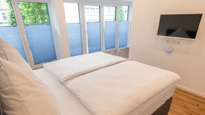 Ein Schlafzimmer mit einem großen Bett, Holzboden und einem an der Wand befestigten Fernseher.