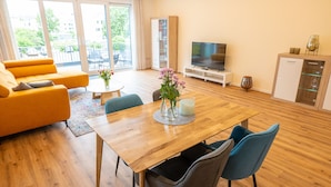 Ein modernes Wohnzimmer mit Holzboden, einem Esstisch mit Stühlen, einer Couch, einem Fernseher und einem Schrank.