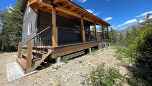 Une cabane en bois dotée d’un porche, construite sur un terrain rocheux et entourée d’arbres.
