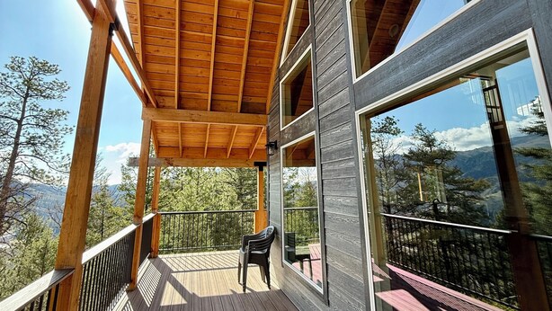 Une terrasse en bois agrémentée d’une pergola, de grandes fenêtres et offrant une vue sur un paysage montagneux.