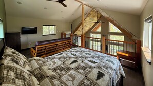 Une chambre avec un grand lit, un banc en bois, un ventilateur de plafond, une télévision et un escalier menant à un niveau supérieur.