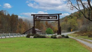 A wooden sign with 'SNOWSHOE Forever Wild' written on it, a gravel path, a wooden fence, and a backdrop of autumn-colored trees. - ML 340: Amazing lift & mountain views, new deck + AC! (Snowshoe)