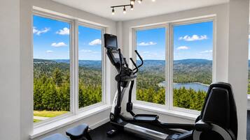 A home gym with a treadmill, stationary bike, and elliptical machine, featuring large windows with a scenic view.