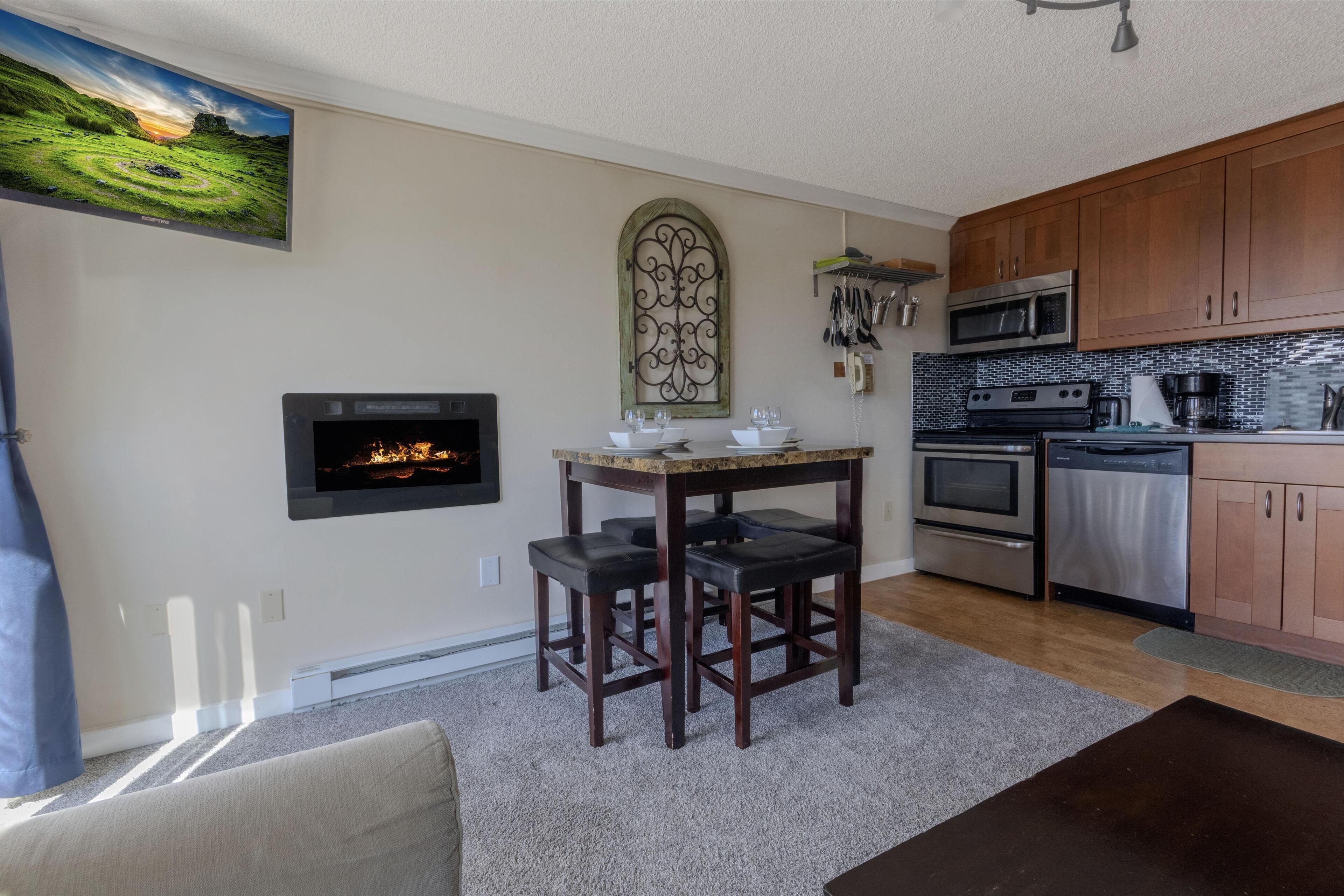 A modern kitchen with wooden cabinets, stainless steel appliances, a fireplace, and a dining area with a table and chairs.