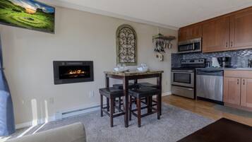 A modern kitchen with wooden cabinets, stainless steel appliances, a fireplace, and a dining area with a table and chairs.