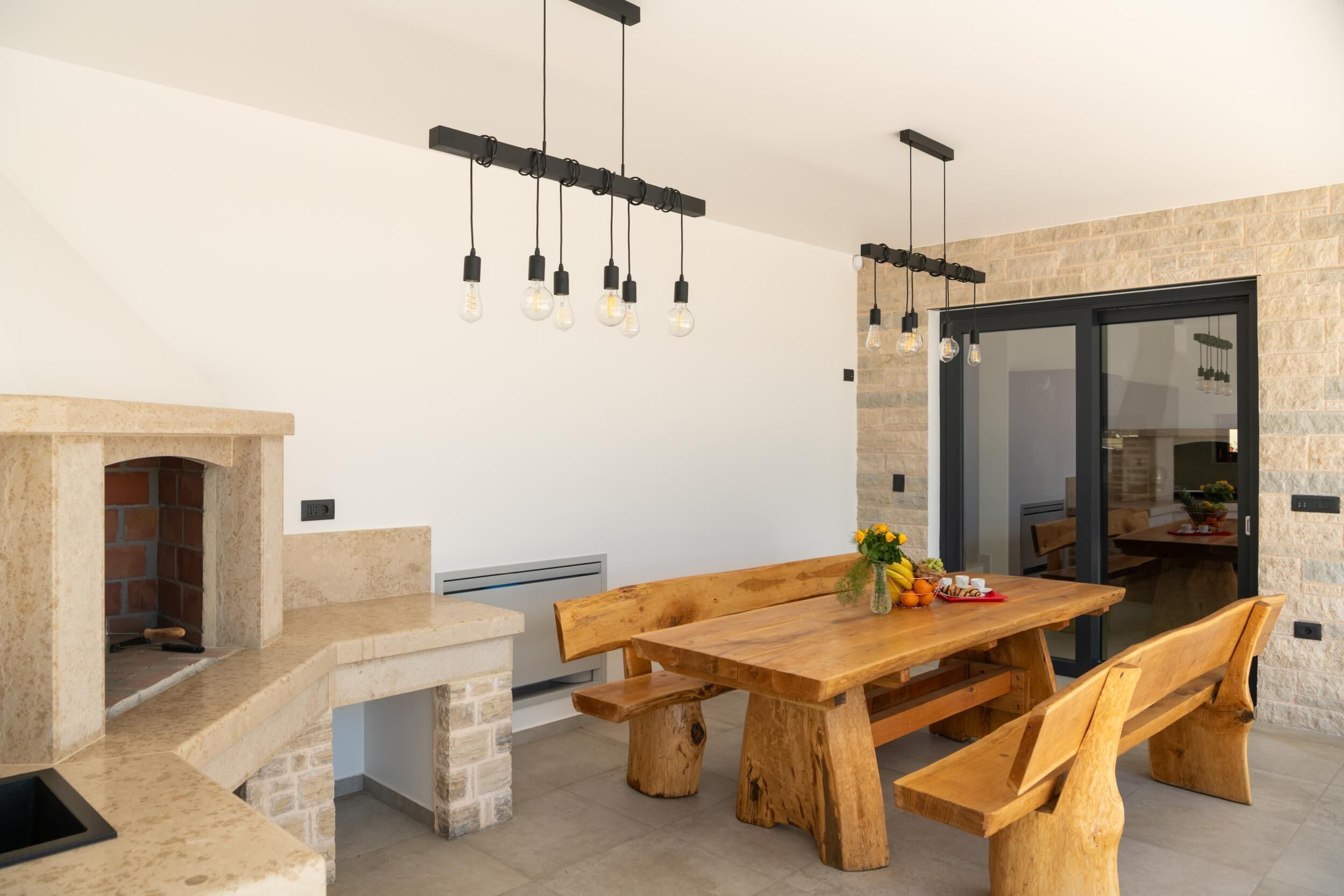 Een moderne keuken met een steenschild achter de kookplaat, een ingebouwde oven en een houten eettafel met banken.