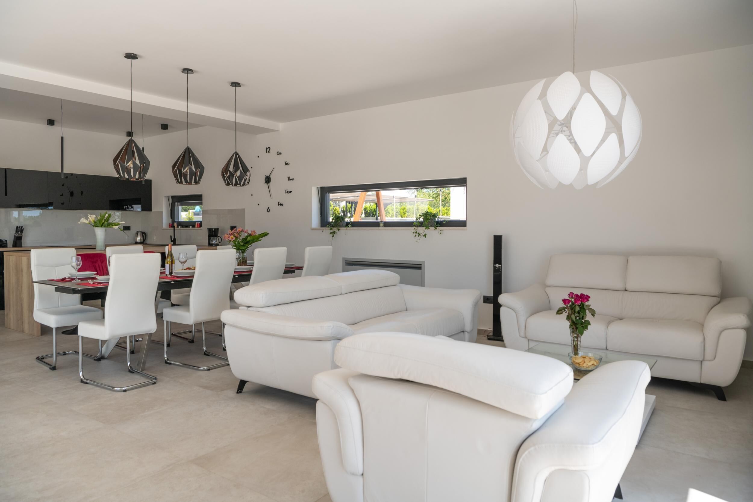 A modern living room with a sectional sofa, dining area with white chairs, and a kitchen in the background.
