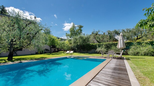 Una piscina con cubierta de madera, rodeada de follaje y un cielo despejado.