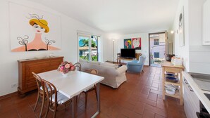 Una sala de estar con un sofá, una mesa de comedor con sillas, un televisor y obras de arte en las paredes.